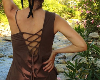 May include: A brown sleeveless top with a lace-up back detail. The top is worn by a person with long black hair, standing in a natural setting.