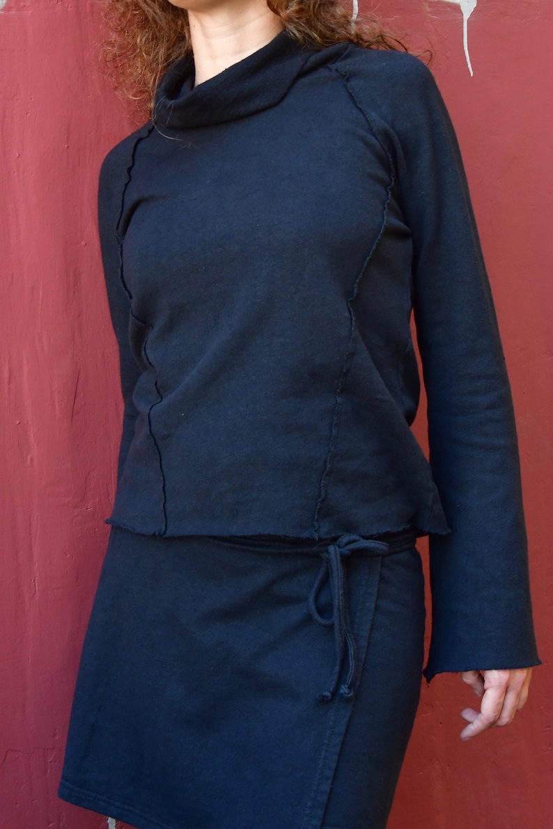 May include: A black mock neck shirt with long sleeves and a wrap skirt. The shirt has a raw edge detail and the skirt has a tie closure.