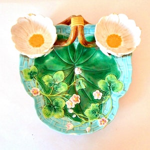 Könnte beinhalten: Eine antike Keramik-Servierplatte mit zwei kleinen Schalen. Die Platte ist mit einem grünen Blattdesign und rosa Blumen verziert. Die Schalen sind weiß mit rosa und gelben Akzenten.