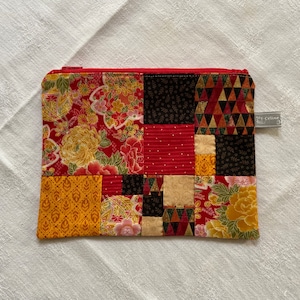 Peut inclure: Une pochette zippée en tissu patchwork rouge, jaune et noir avec un motif floral. La pochette porte une étiquette "Et Celine".