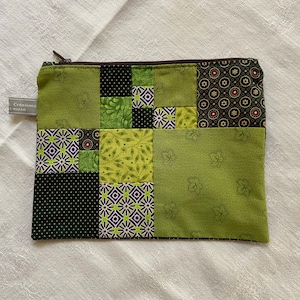 Peut inclure: Une pochette zippée en patchwork dans les tons de vert, noir et violet. Le motif présente des carrés de tissu à motifs, notamment des imprimés floraux et géométriques. Une petite étiquette avec du texte est attachée sur le côté.