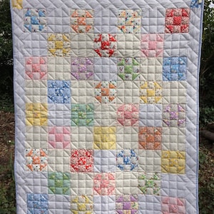 Peut inclure: Une courtepointe en patchwork avec une variété de motifs floraux dans des tons de rose, bleu, jaune et vert. La courtepointe est faite de carrés et est matelassée avec un motif en losange.