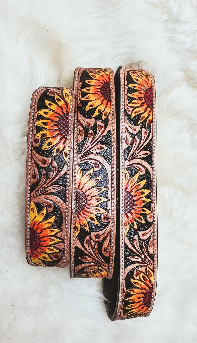 May include: Three leather belts with sunflower designs. The belts are brown with black accents and feature yellow, orange, and red sunflowers.