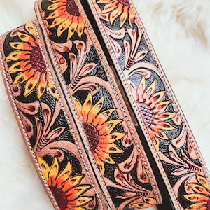 May include: Three leather belts with sunflower and floral designs. The belts are brown with black accents and have a stitched edge.