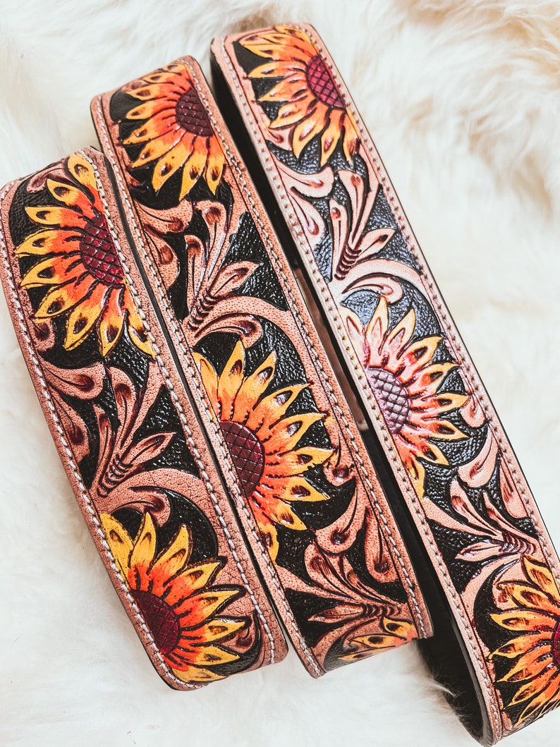 May include: Three leather belts with sunflower and floral designs. The belts are brown with black accents and have a stitched edge.