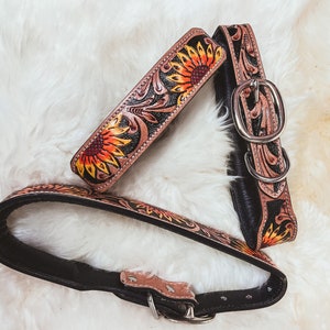 May include: Two leather dog collars with a sunflower design. One collar is black with a sunflower pattern, and the other is brown with a sunflower pattern.
