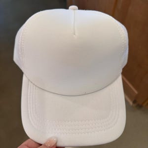 Peut inclure: Un chapeau de camionneur blanc avec un dos en mesh. Le chapeau a une visière plate et est fait d'un matériau doux et respirant.