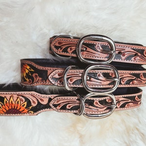 May include: Three leather dog collars with floral and sunflower designs. The collars are black with brown floral accents and silver buckles.