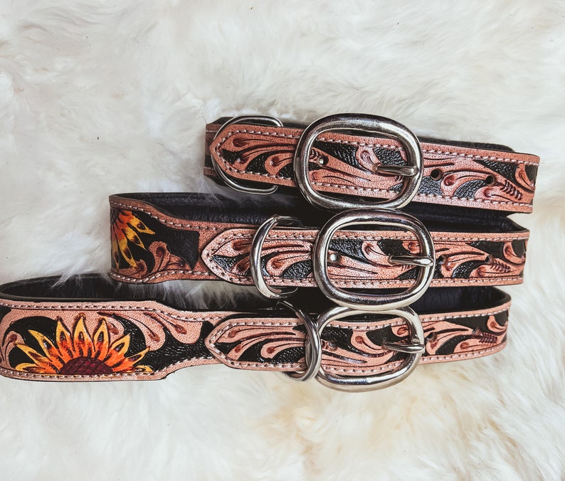 May include: Three leather dog collars with floral and sunflower designs. The collars are black with brown floral accents and silver buckles.