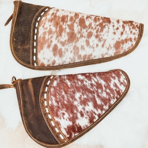May include: Two brown leather gun holsters with a white and brown cowhide pattern. The holsters have a stitched design around the edges.
