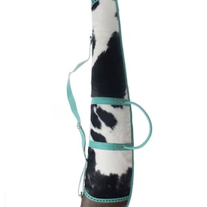 Puede incluir: Una funda para rifle de piel de vaca en blanco y negro con detalles en piel turquesa y una correa para el hombro.