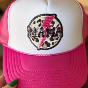 May include: Pink and white trucker hat with a black and white leopard print patch that says "MAMA" in pink glitter letters with a pink lightning bolt.
