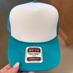 May include: A turquoise and white trucker hat with a black label that reads "OTTO World Famous Foam Front OSFM Trucker Durable Snap Closure".