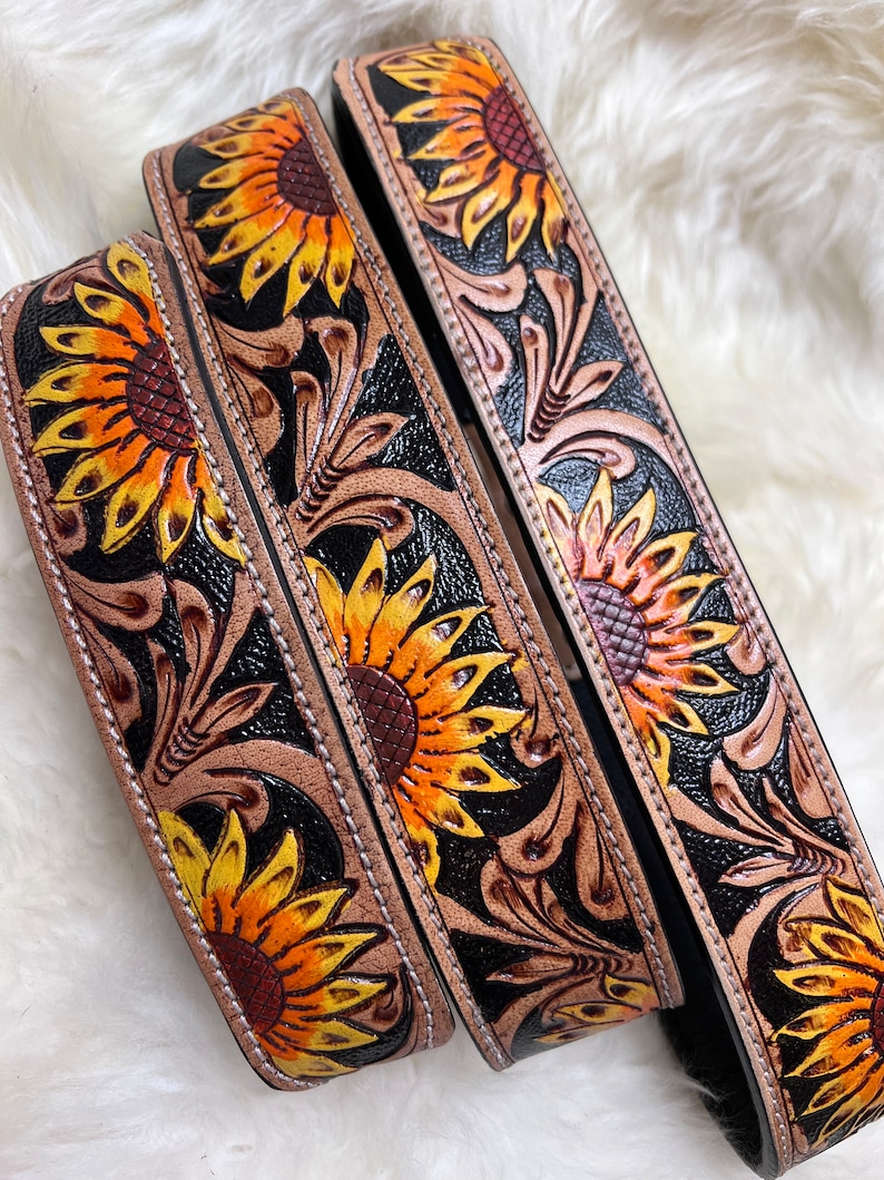 May include: Three leather belts with sunflower designs. The belts are black with brown leather tooling and yellow and orange sunflowers.