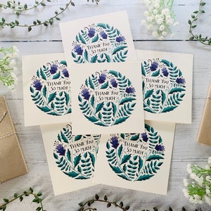 May include: Six thank you cards with a floral design featuring purple flowers and green leaves. The cards have the text "Thank You So Much" printed on them.