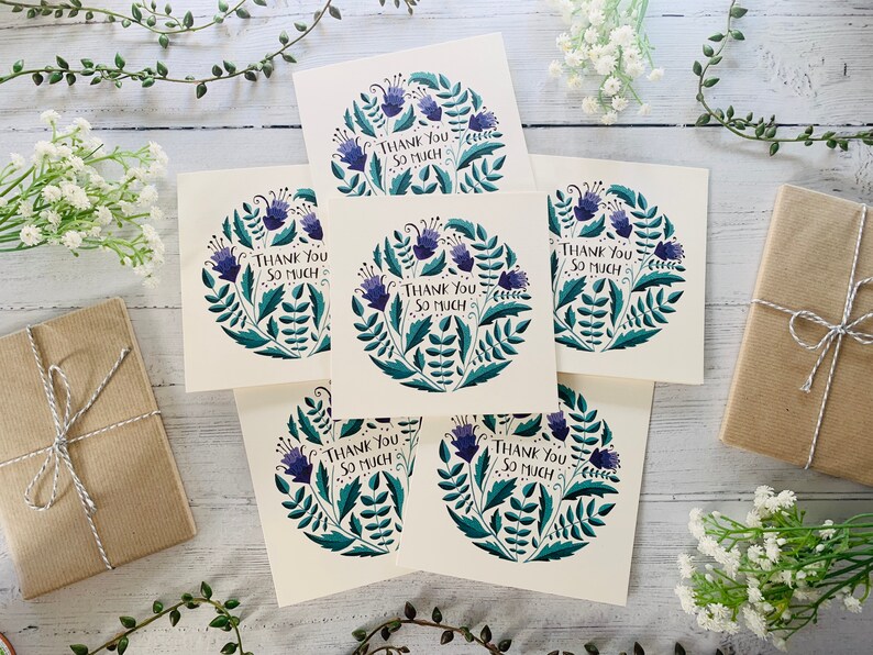 May include: Six thank you cards with a floral design featuring purple flowers and green leaves. The cards have the text "Thank You So Much" printed on them.