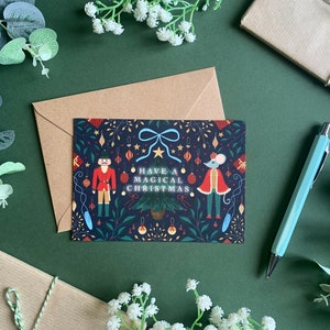 May include: A Christmas card with a dark blue background featuring a nutcracker and a mouse in festive attire. The card has a white border and the text "Have a Magical Christmas" in white letters.