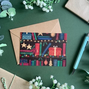 May include: A Christmas card featuring a bookshelf with books, lights, and ornaments. The books have titles like "The Nutcracker" and "A Christmas Carol".