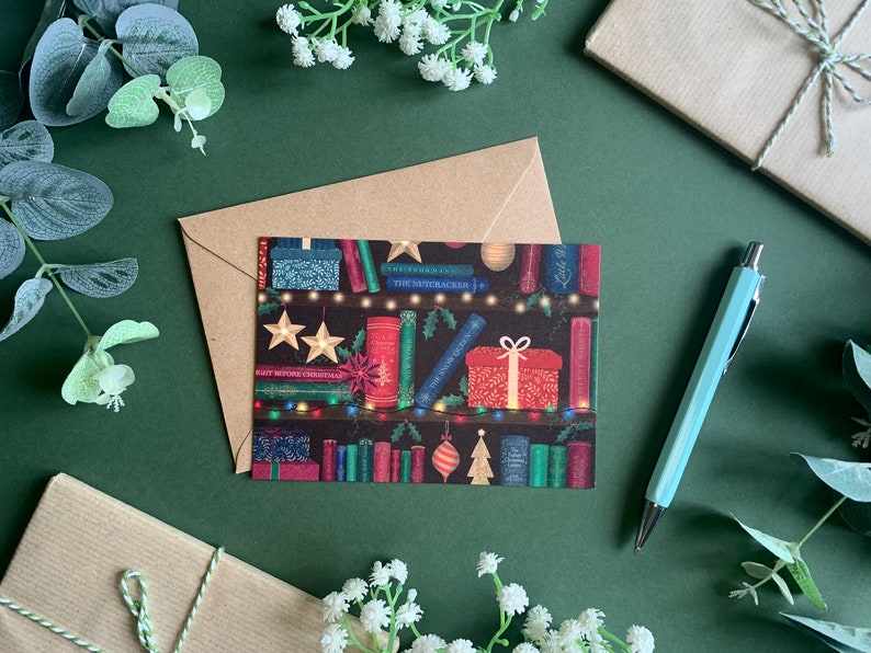 May include: A Christmas card featuring a bookshelf with books, lights, and ornaments. The books have titles like "The Nutcracker" and "A Christmas Carol".