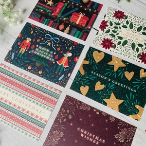 May include: Assortment of Christmas cards with various festive designs. The cards feature illustrations of a nutcracker, a mouse, gingerbread cookies, poinsettias, and a Christmas tree. The cards have different greetings, including "Merry Christmas", "Season's Greetings", and "Have a Magical Christmas".