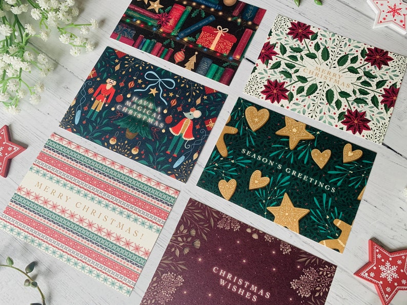 May include: Assortment of Christmas cards with various festive designs. The cards feature illustrations of a nutcracker, a mouse, gingerbread cookies, poinsettias, and a Christmas tree. The cards have different greetings, including "Merry Christmas", "Season's Greetings", and "Have a Magical Christmas".