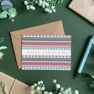 May include: A Christmas card with a red, green, and blue patterned design. The card says "Merry Christmas!" in gold lettering.