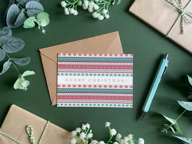 May include: A Christmas card with a red, green, and blue patterned design. The card says "Merry Christmas!" in gold lettering.
