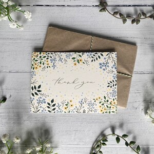 Puede incluir: Una tarjeta blanca con un borde floral en tonos azules y amarillos. La tarjeta dice "Gracias" en una fuente manuscrita.