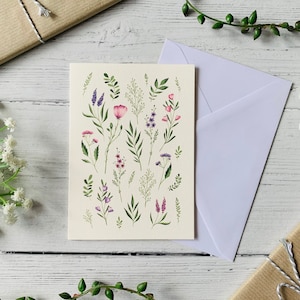 K&ouml;nnte beinhalten: Eine wei&szlig;e Karte mit einer Aquarell-Illustration von rosa und lila Blumen und gr&uuml;nen Bl&auml;ttern. Die Karte ist leer und bereit f&uuml;r eine Nachricht.