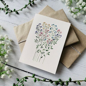 K&ouml;nnte beinhalten: Eine wei&szlig;e Karte mit einer Aquarell-Illustration eines Strau&szlig;es kleiner Blumen in Rosa-, Blau- und Gelbt&ouml;nen. Die Blumen sind in einem lockeren, nat&uuml;rlichen Stil angeordnet.
