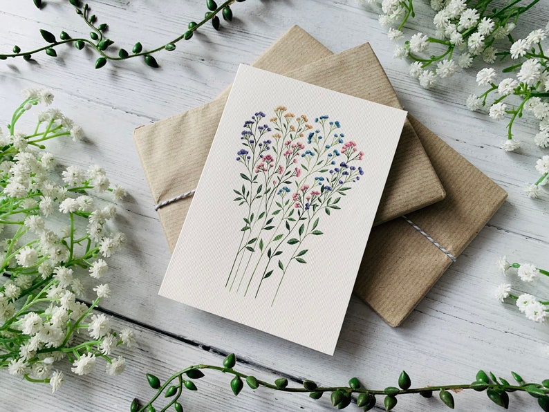 K&ouml;nnte beinhalten: Eine wei&szlig;e Karte mit einer Aquarell-Illustration eines Strau&szlig;es kleiner Blumen in Rosa-, Blau- und Gelbt&ouml;nen. Die Blumen sind in einem lockeren, nat&uuml;rlichen Stil angeordnet.