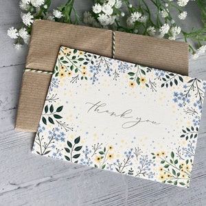 Puede incluir: Una tarjeta blanca con un borde floral de flores amarillas y azules. La tarjeta dice "Gracias" en escritura cursiva.