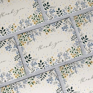 Puede incluir: Un conjunto de cinco tarjetas de agradecimiento con un dise&ntilde;o floral. Las tarjetas son blancas con un patr&oacute;n floral azul claro y amarillo y las palabras "Gracias" escritas en cursiva negra.