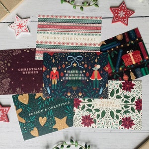 May include: Assortment of six Christmas cards with various festive designs. The cards feature illustrations of a nutcracker, a mouse, a Christmas tree, and a poinsettia. The cards have different greetings, including "Merry Christmas!" and "Have a Magical Christmas."