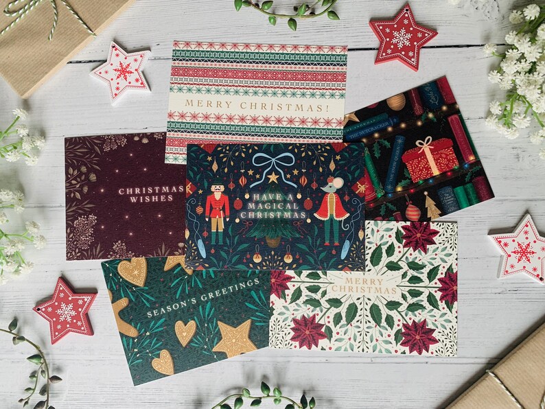May include: Assortment of six Christmas cards with various festive designs. The cards feature illustrations of a nutcracker, a mouse, a Christmas tree, and a poinsettia. The cards have different greetings, including "Merry Christmas!" and "Have a Magical Christmas."