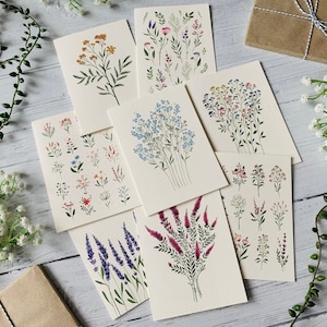 K&ouml;nnte beinhalten: Satz von acht Karten mit verschiedenen Blumenillustrationen. Die Karten sind wei&szlig; mit schwarzer Tinte und zeigen verschiedene Blumen, darunter blaue Vergissmeinnicht, rosa und violette Wildblumen, gelbe Wildblumen und Lavendel.