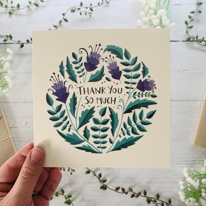 May include: A thank you card with a circular design featuring purple flowers and green leaves. The text "Thank You So Much" is written in the centre of the card.