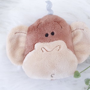 May include: A brown and beige plush monkey toy with a gray tail. The monkey has large ears and a smiling face.