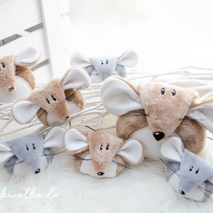 Puede incluir: Un grupo de siete juguetes de ratón de peluche en varios tonos de gris y marrón. Los ratones tienen orejas blancas y ojos negros. Los ratones están dispuestos sobre una superficie blanca y esponjosa con ramas blancas.