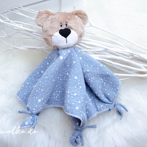 May include: A blue and white muslin baby comforter with a brown bear head attached. The comforter has white polka dots on a light blue background. The bear has black eyes and a black nose.