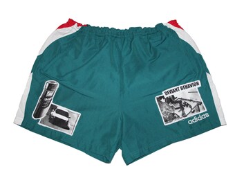 May include: Teal athletic shorts with white and red trim. The shorts have two black and white graphic patches, one with a car and the other with the text "Deviant Behavior" and the Adidas logo.