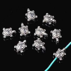 May include: Nine silver turtle charms featuring intricate shell designs. The charms are small and ideal for jewellery making or adding a touch of whimsy to crafts.