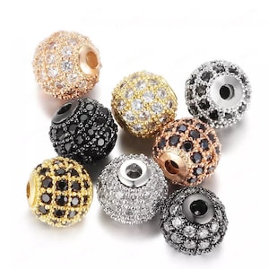 May include: Assortment of round beads with a variety of finishes, including gold, silver, and black. Each bead is covered in small, sparkling rhinestones.