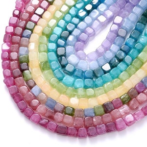 May include: A collection of square-shaped gemstone beads in various colors, including pink, purple, blue, green, and yellow. The beads are arranged in a circular pattern, with the pink beads at the bottom and the yellow beads at the top.