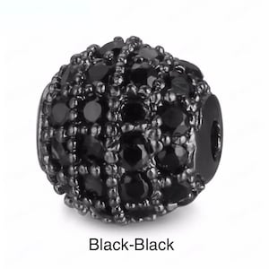 May include: Black bead with a round shape and a black, sparkly finish. The bead is covered in small, black stones.