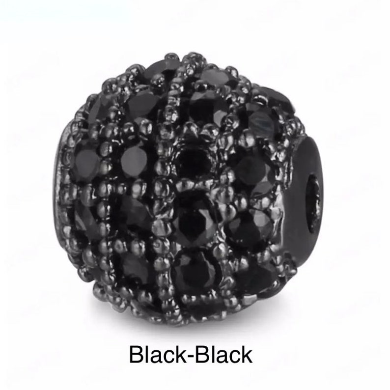May include: Black bead with a round shape and a black, sparkly finish. The bead is covered in small, black stones.