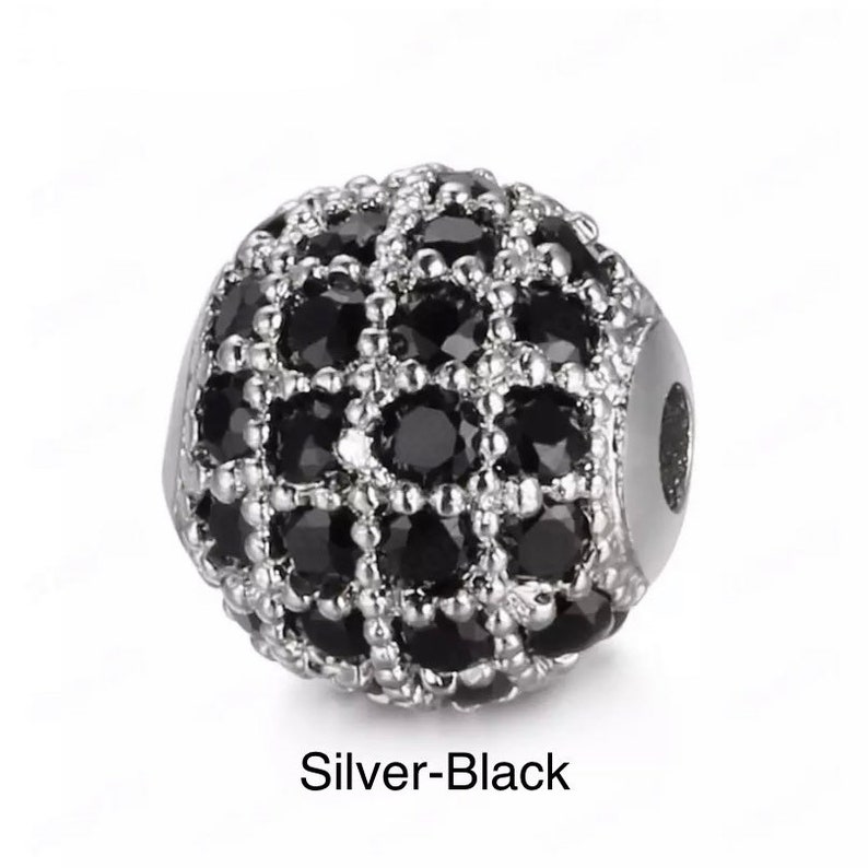 May include: A silver and black round bead with a geometric design. The bead is covered in small black stones.