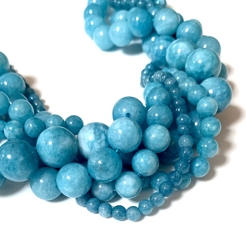 May include: A strand of light blue aquamarine beads in various sizes. The beads are round and smooth, and they are arranged in a loose, flowing pattern.