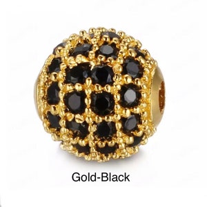 May include: A gold and black round bead with a decorative design of small black stones. The bead has a hole in the center for stringing.
