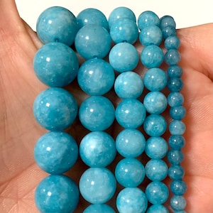 May include: A strand of light blue aquamarine beads in various sizes. The beads are round and smooth, with a slightly cloudy appearance.